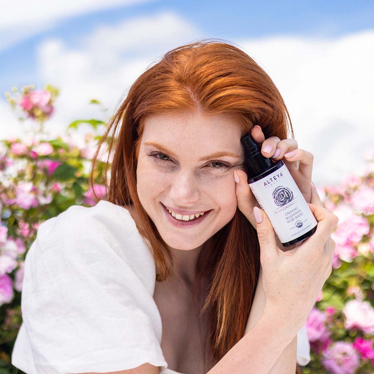 bulgarisches Rosenwasser im violetten Glas mit einem Modell von Alteya Organics